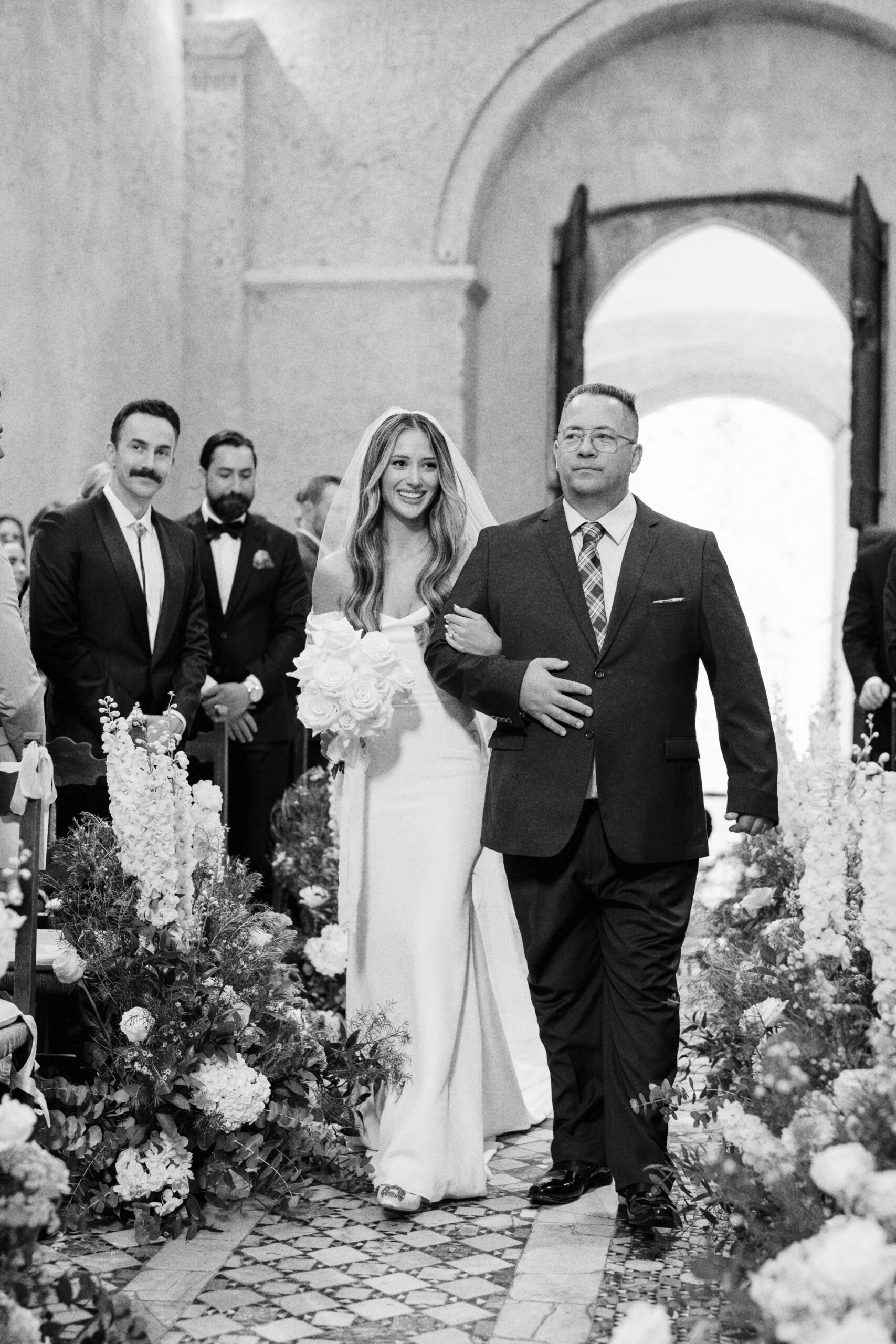 A black and white portrait of bride and her father in the church's aisle of La Badia di Orvieto, Destination wedding venue in Umbria